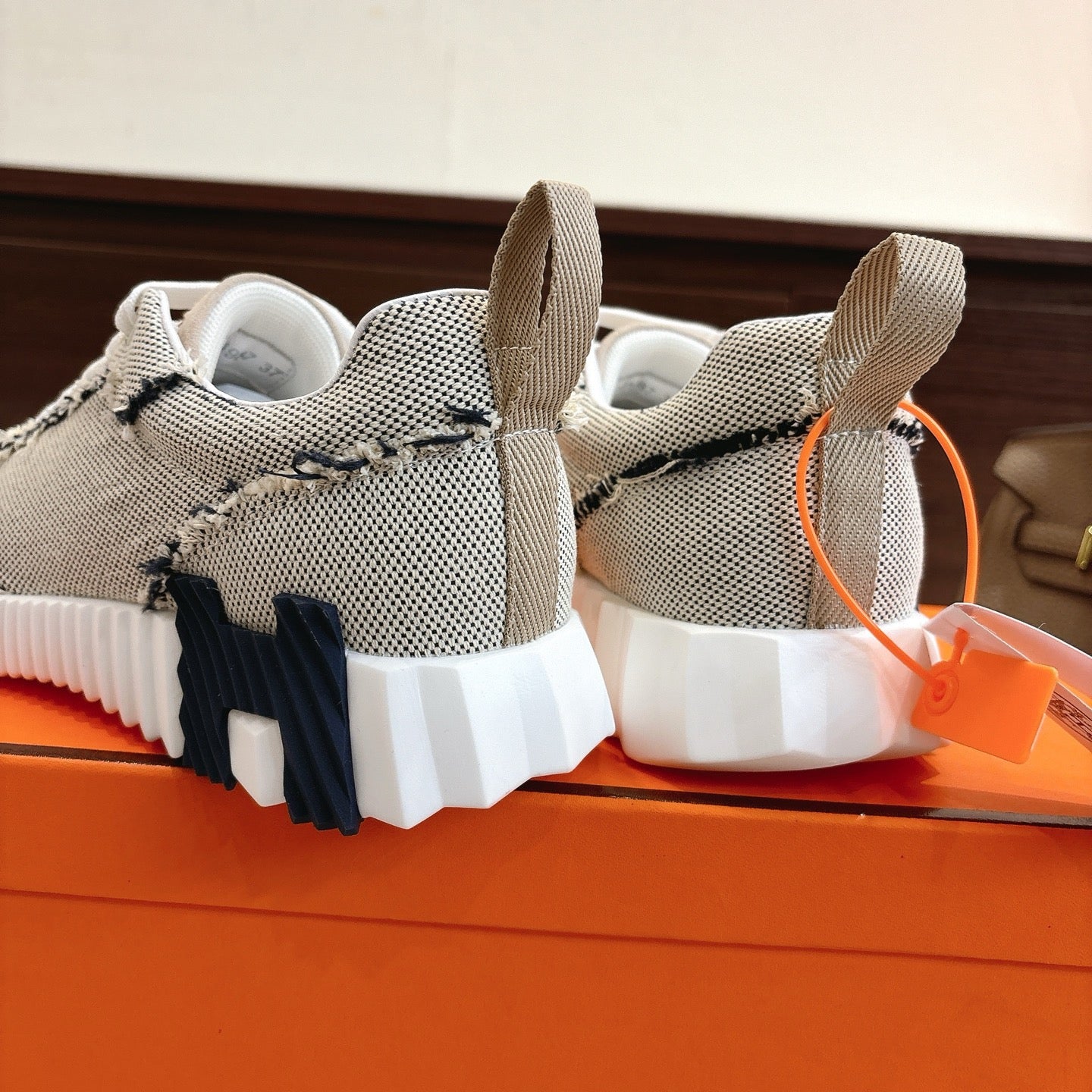 Hermes sneakers heel view: light mesh, navy panel detail, chunky white sole, pull tabs.