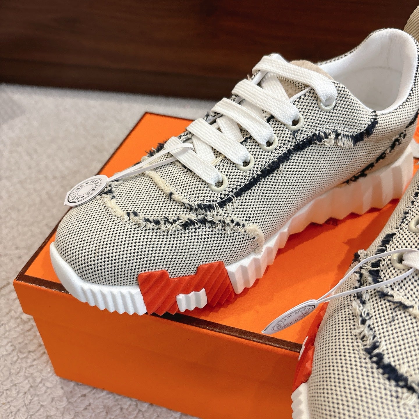Hermes sneakers close-up: light mesh with navy trim, white laces, textured tread sole.