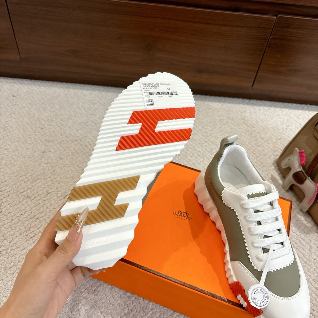 Shoe outsole view with orange strip, white and olive sneaker with side logo badge.
