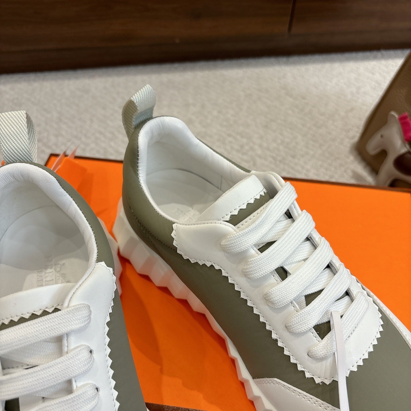 Close-up of white unisex sneaker upper with white laces and side logo badge on olive panel.