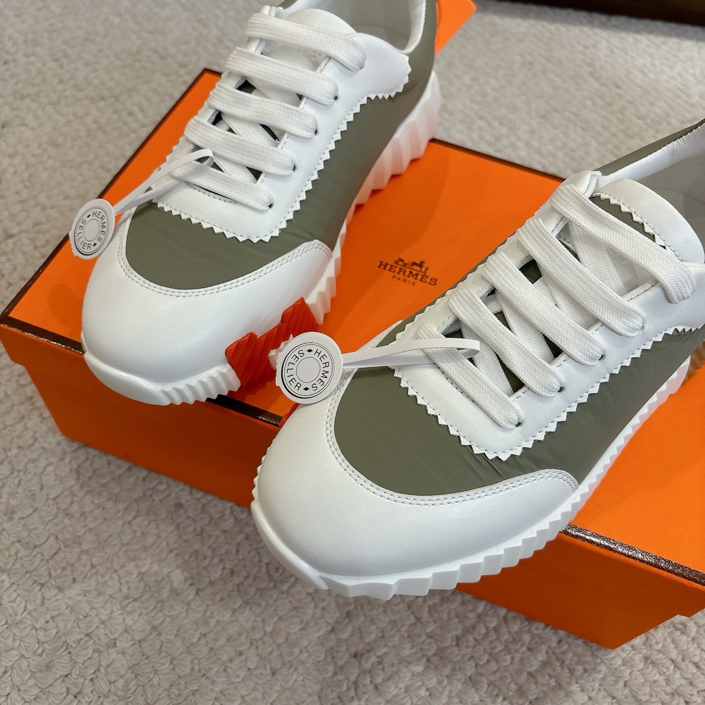 Two white and olive unisex sneakers with white laces, scalloped trim, side logo badge.