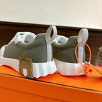 Back view of white and olive unisex sneakers on chunky sole with orange pull tab.