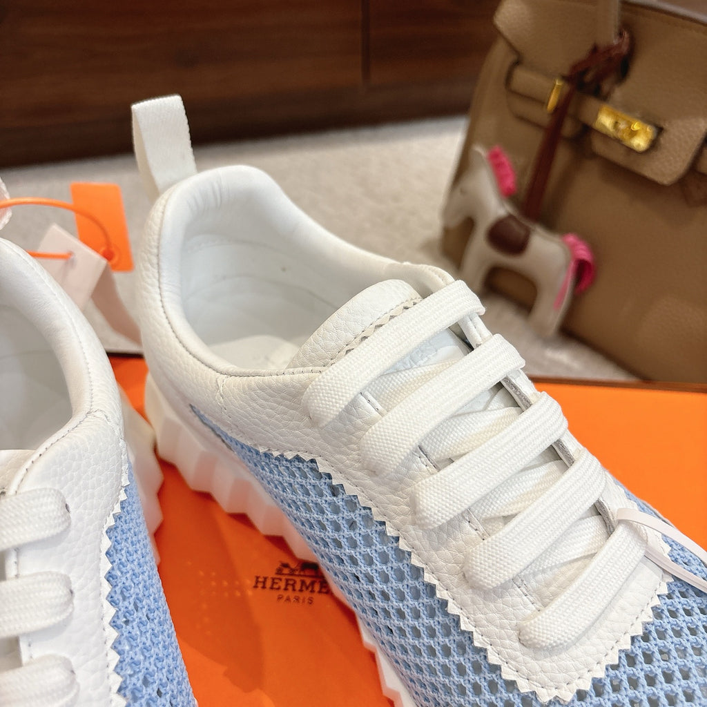 Hermes unisex luxury sneakers, close-up of white laces over light blue panel, round logo patch.