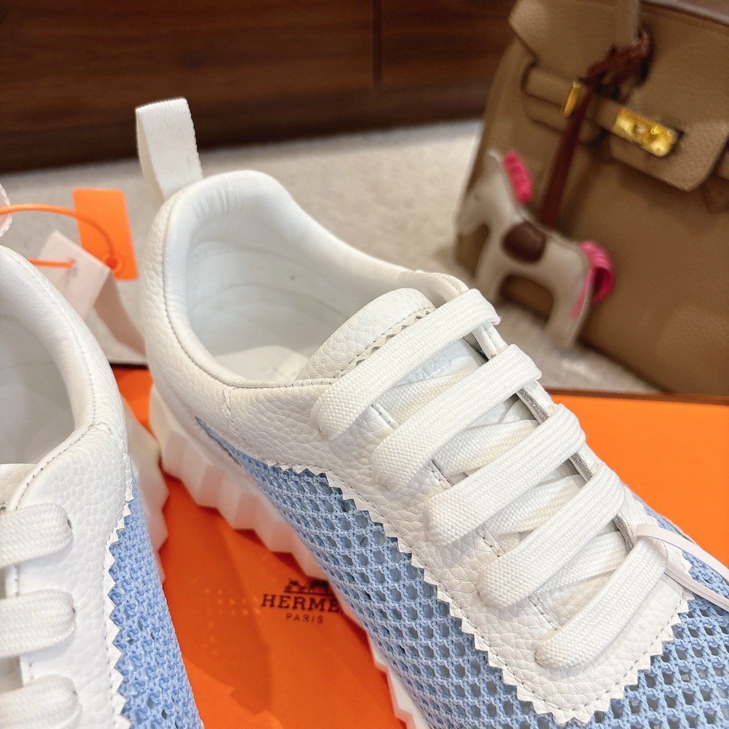 Hermes unisex luxury sneakers, close-up of white laces over light blue panel, round logo patch.