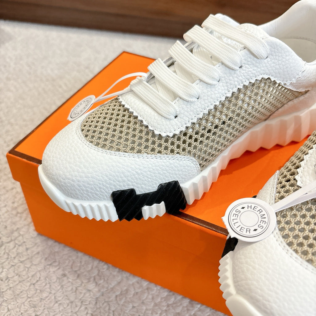 Hermes unisex sneaker close-up, white toe and tan mesh upper with round logo tag.