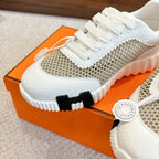 Hermes unisex sneaker close-up, white toe and tan mesh upper with round logo tag.