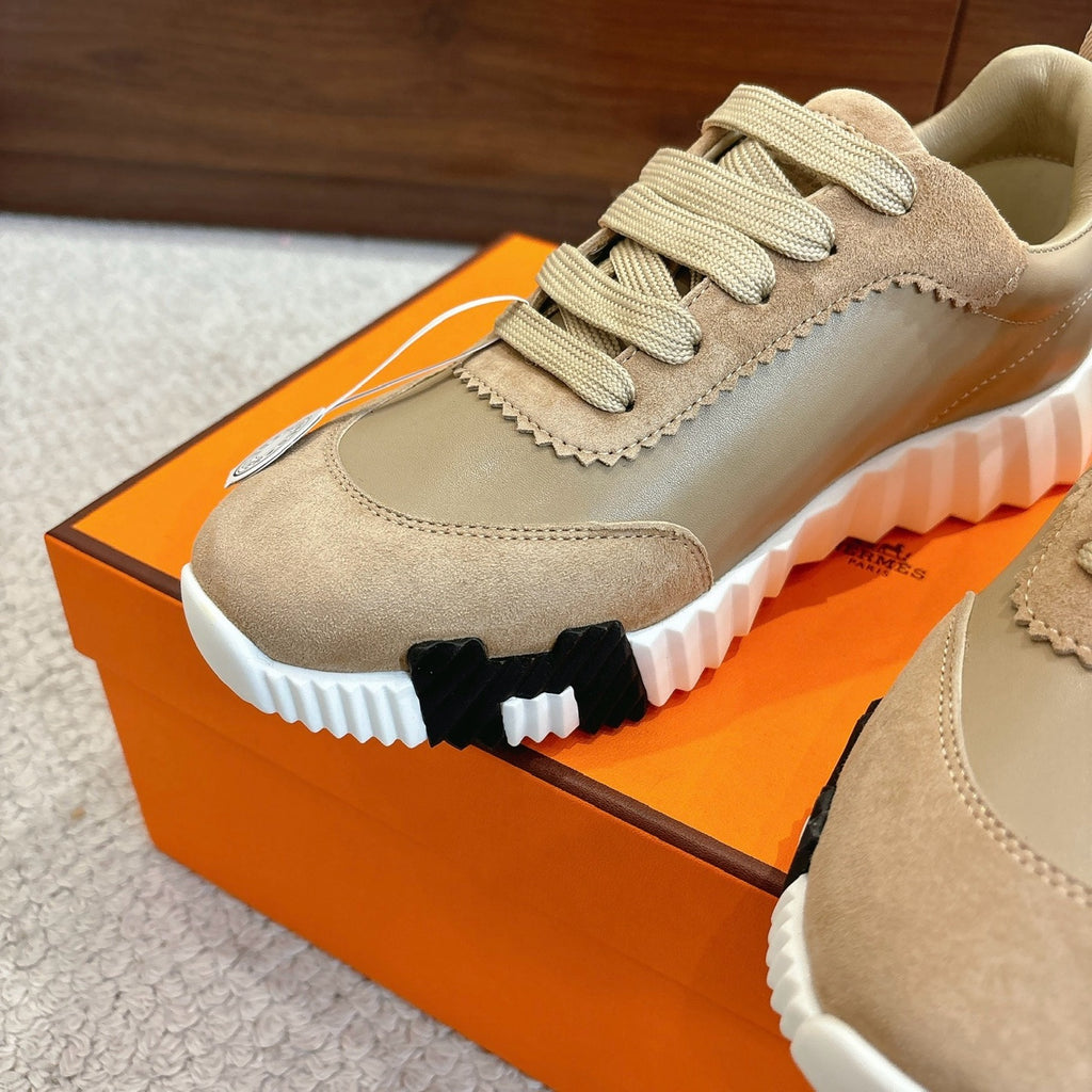 Unisex light tan sneaker close-up with lace-up, textured panels, and chunky white tread sole.