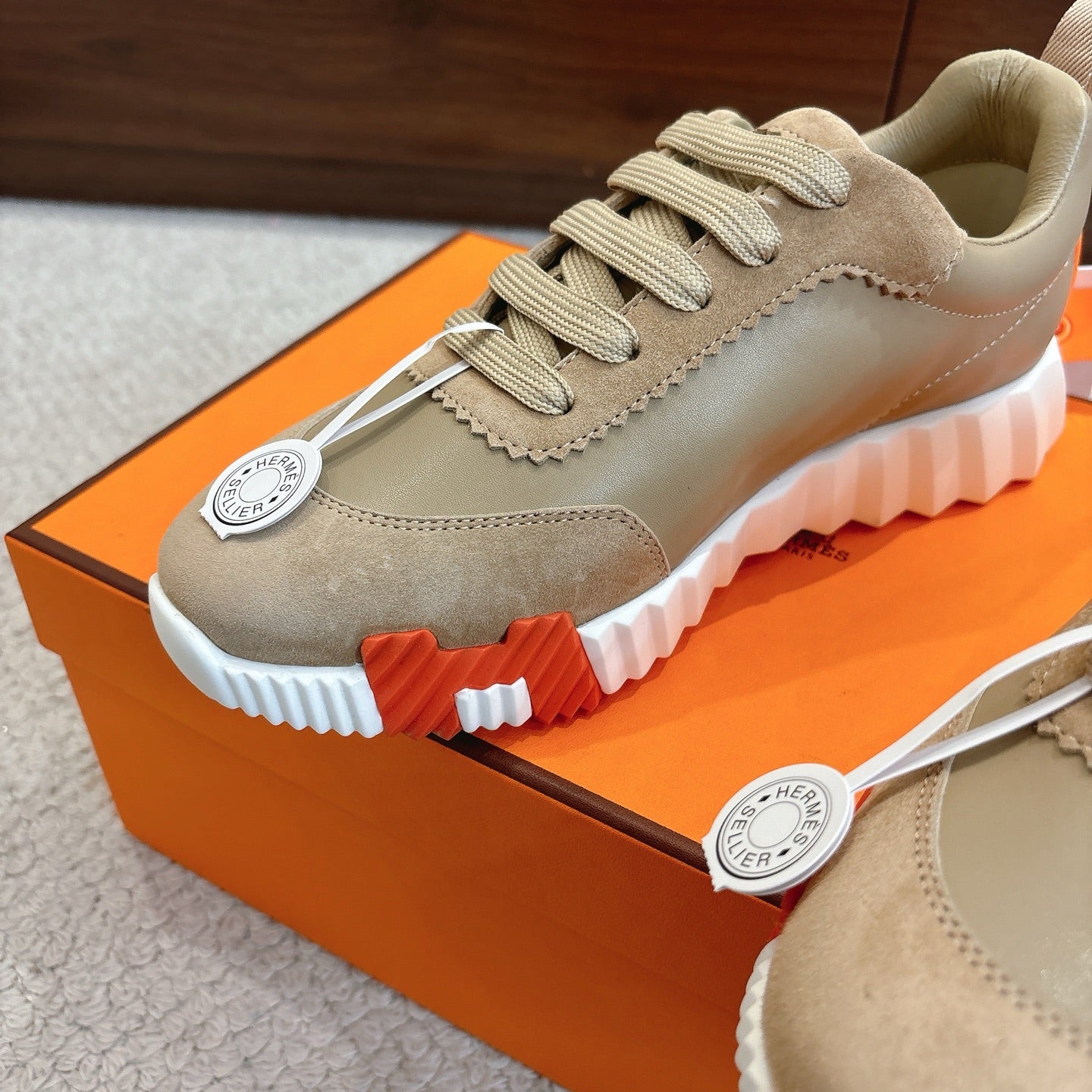 Close-up of beige suede lace-up sneaker with white sole, serrated lugs, logo medallion