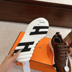 Hermes unisex sneaker outsole view, white rubber tread with black stripes; brown upper.