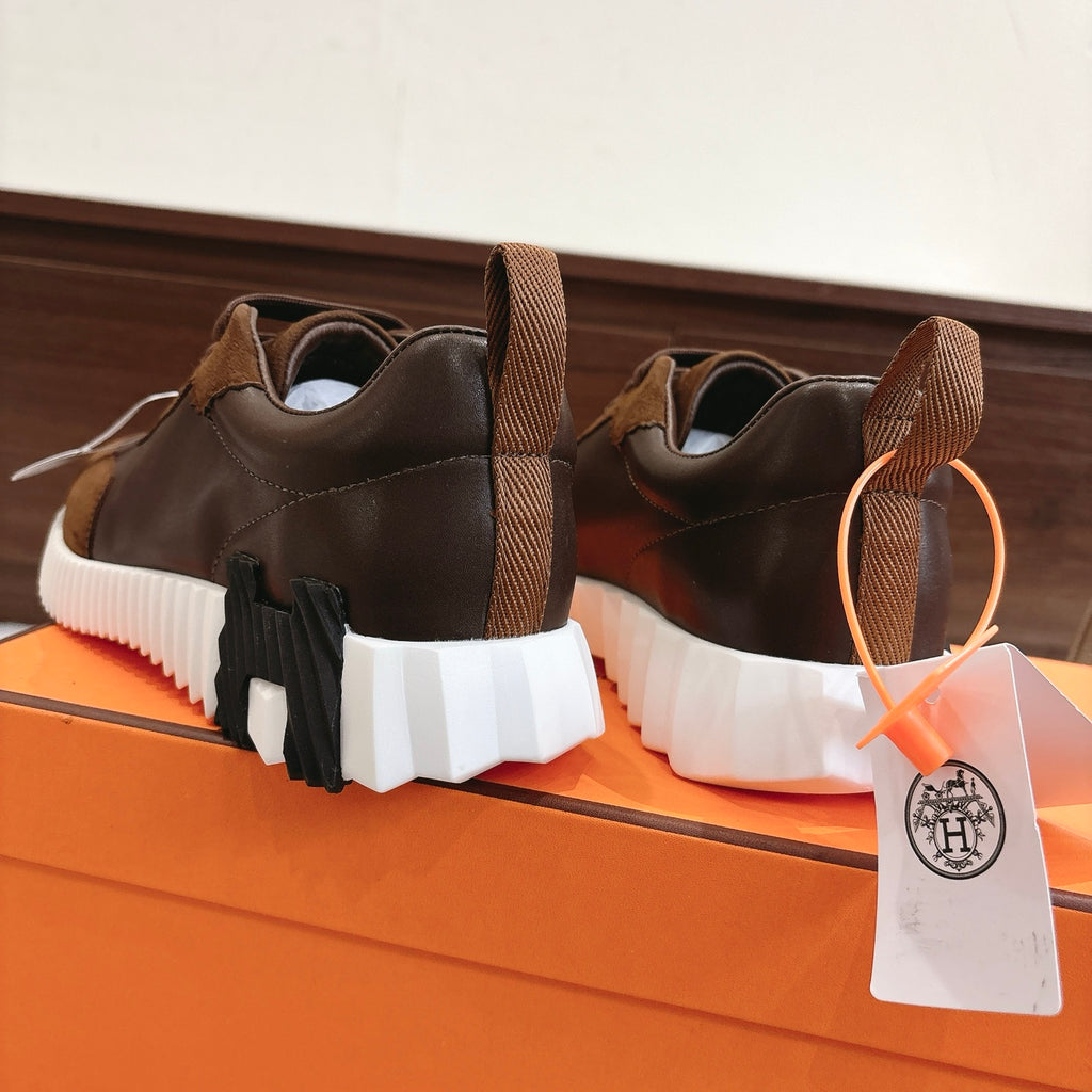 Hermes unisex sneakers rear view, brown uppers with lace-up and orange tag, white segmented sole.