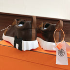 Hermes unisex sneakers rear view, brown uppers with lace-up and orange tag, white segmented sole.