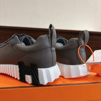 Gray sneakers from rear view with thick white sole and orange lace pull tags