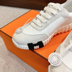Hermes white unisex sneaker close-up, white laces, textured sole edge, round logo tag