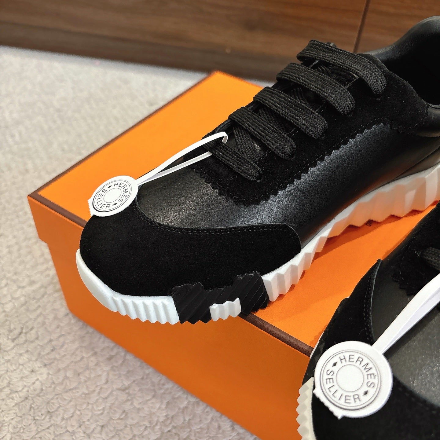 Hermes unisex sneaker detail: black lace-up upper with logo patch and ridged white sole