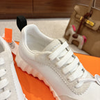 White low-top sneaker close-up with white lace eyelets and scalloped trim along the upper.