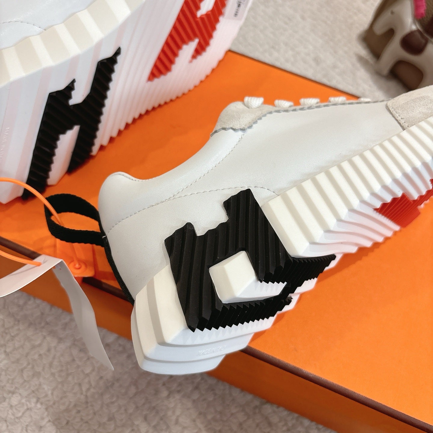 White low-top sneaker outsole close-up with black tread blocks and red accent stripes.