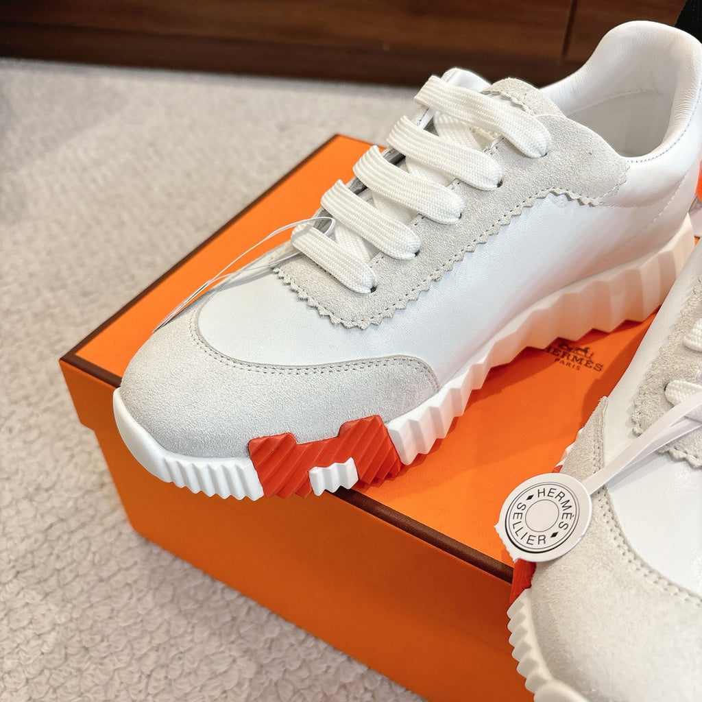 White low-top sneakers close-up showing lace row, suede-like panel, and chunky sole edge.