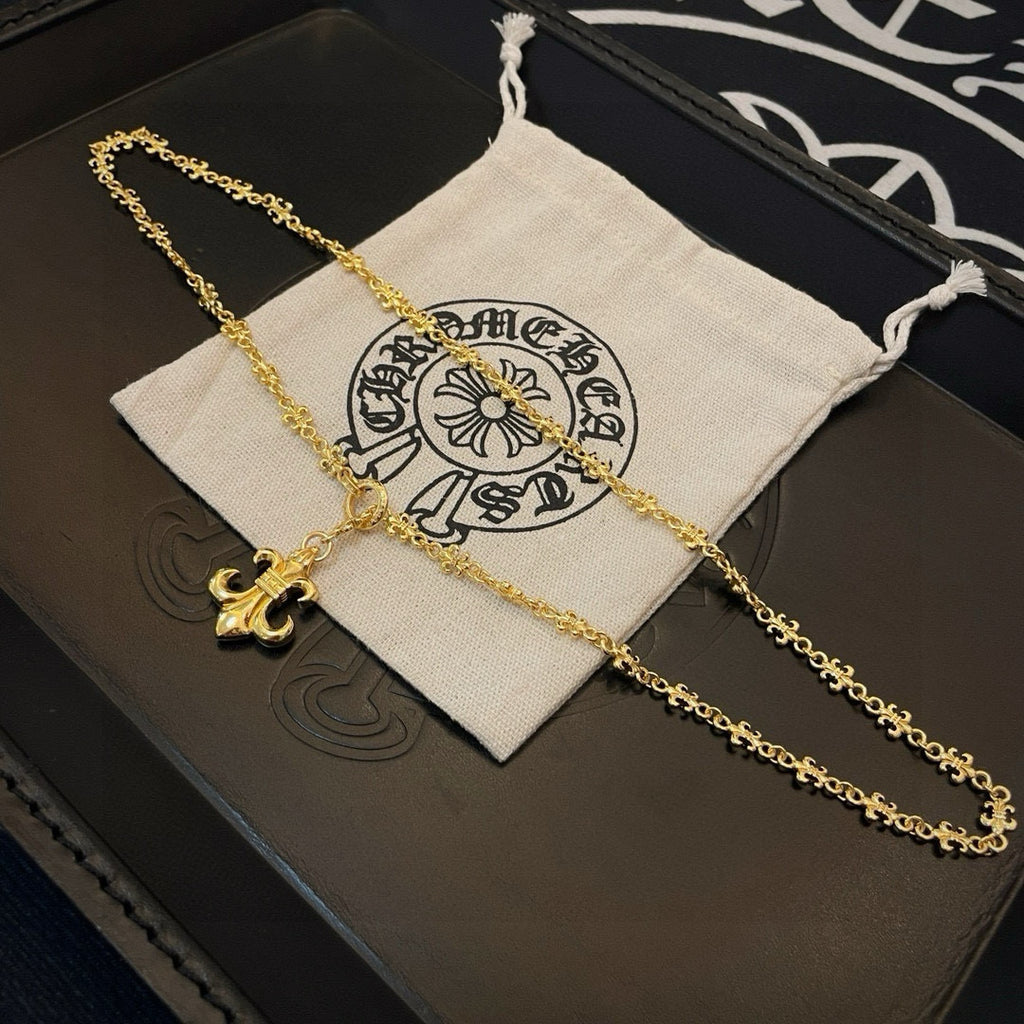 Gold-tone fleur de lis pendant necklace with chain on a small fabric pouch