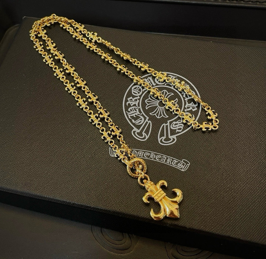 Gold-tone layered chain necklace with fleur de lis pendant on dark jewelry box