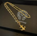 Gold-tone layered chain necklace with fleur de lis pendant on dark jewelry box