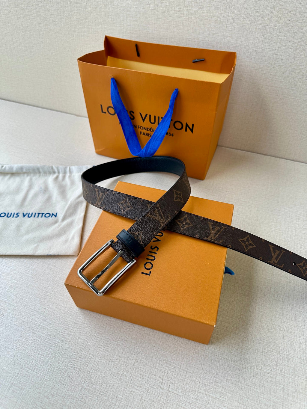 Louis Vuitton monogram belt with silver buckle and dark strap, laid on dust bag