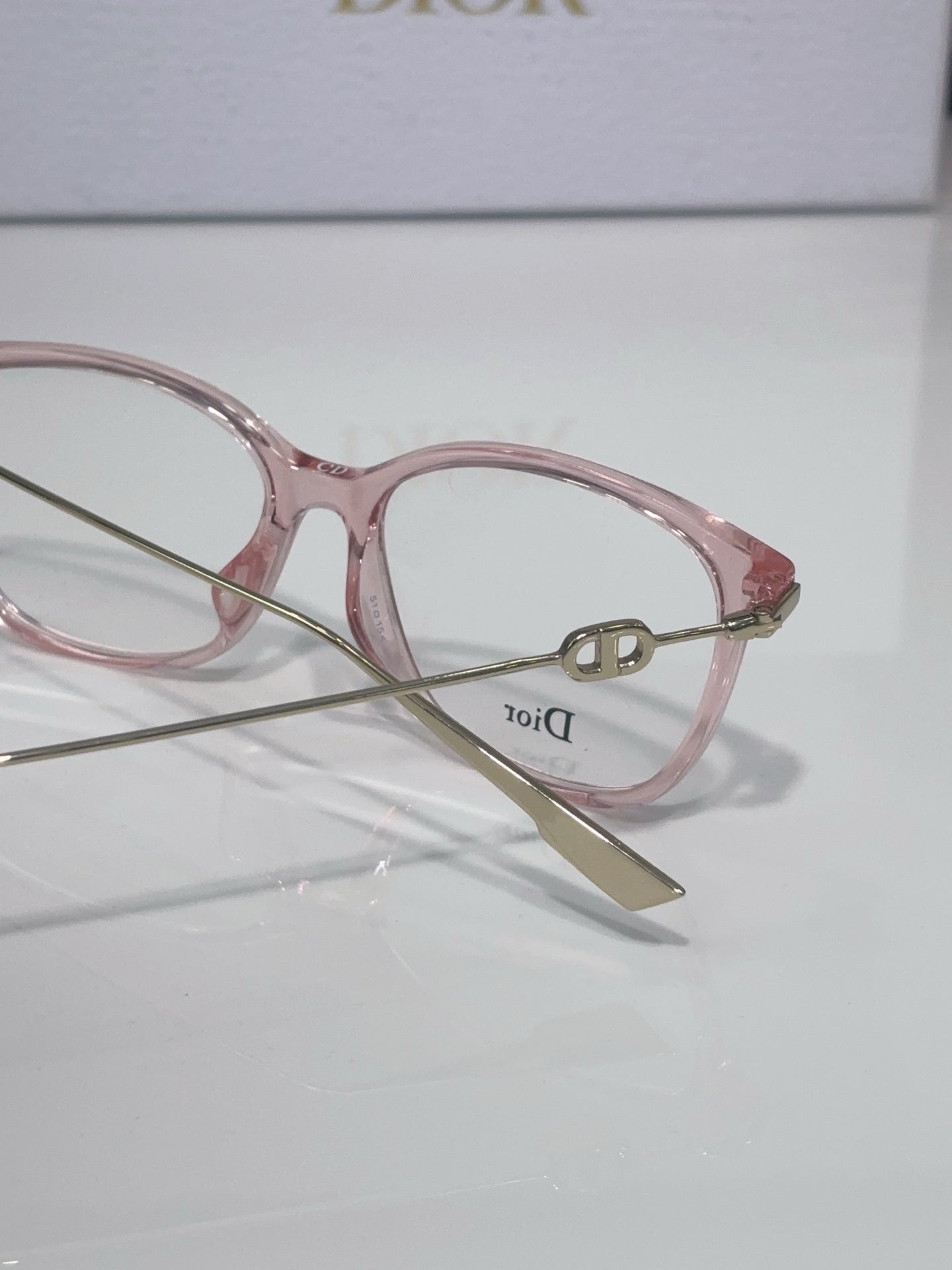 Dior glasses close-up with rose pink frame, gold hinges, and clear lens