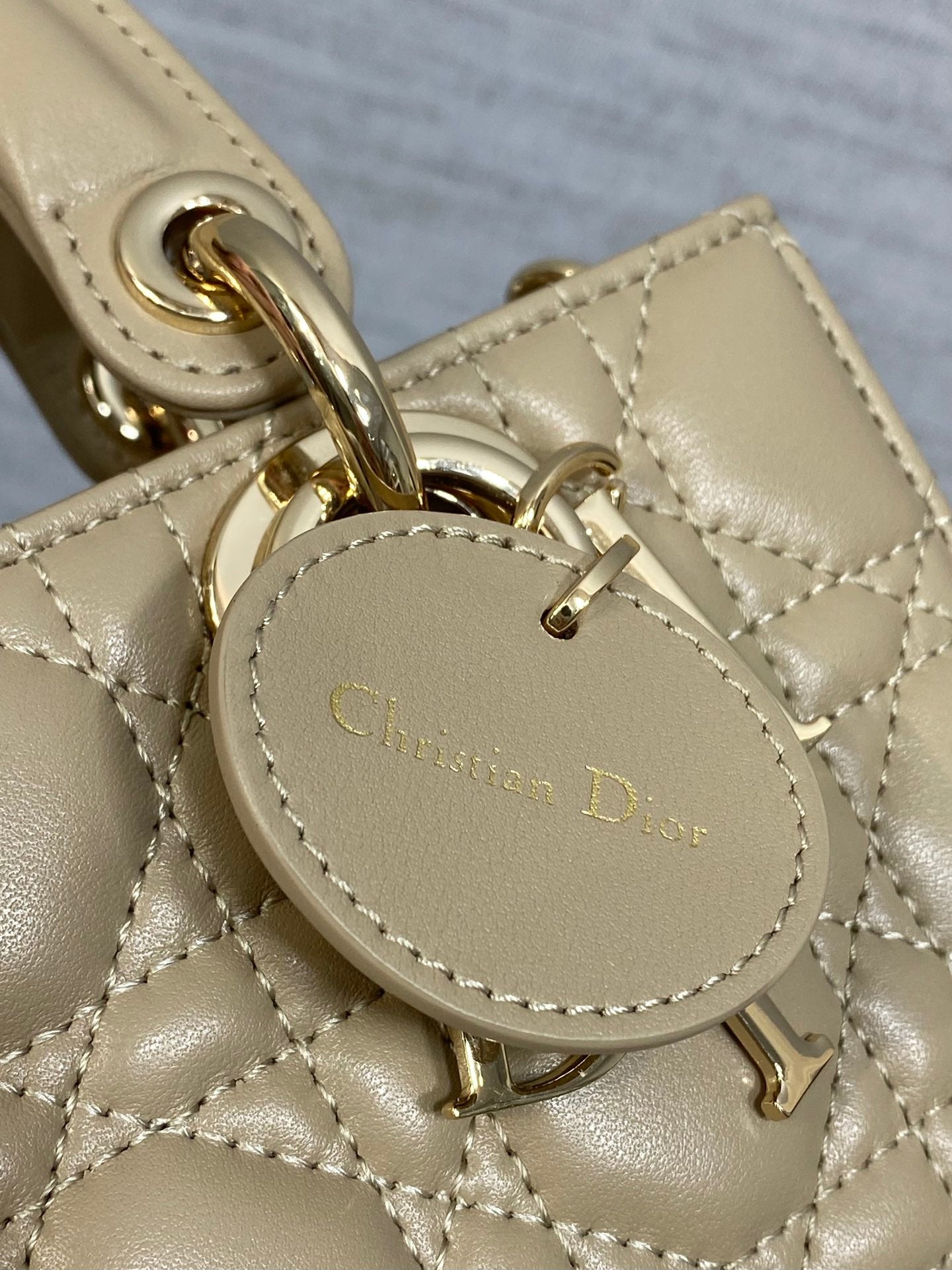 Christian Dior logo tag on quilted beige handbag, with gold-tone hardware