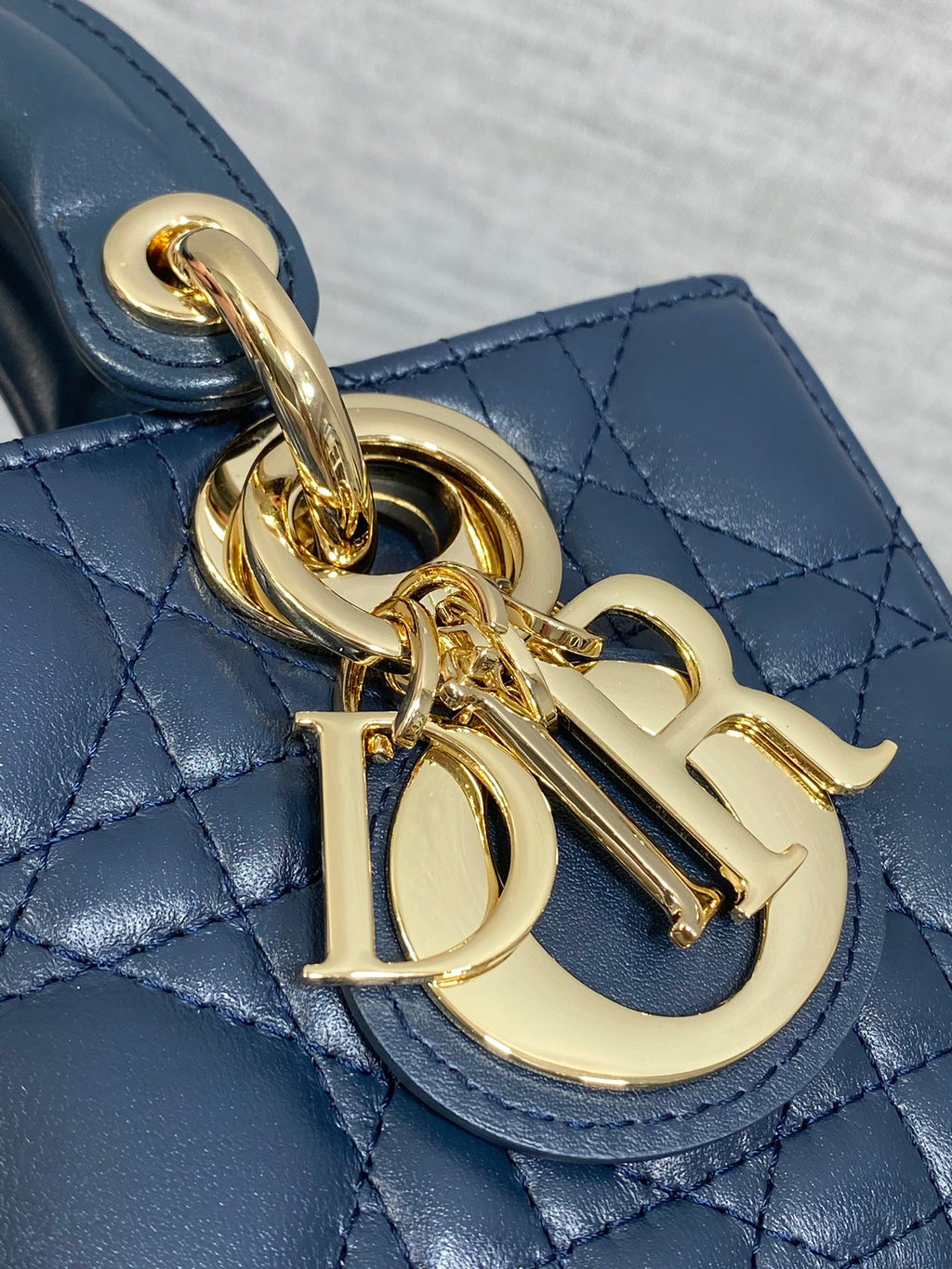 Dior handbag close-up of gold-tone chain charm and D-style logo on navy leather
