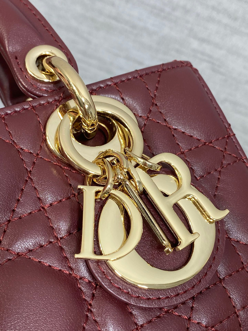 Dior logo charm close-up on burgundy quilted handbag with gold chain hardware