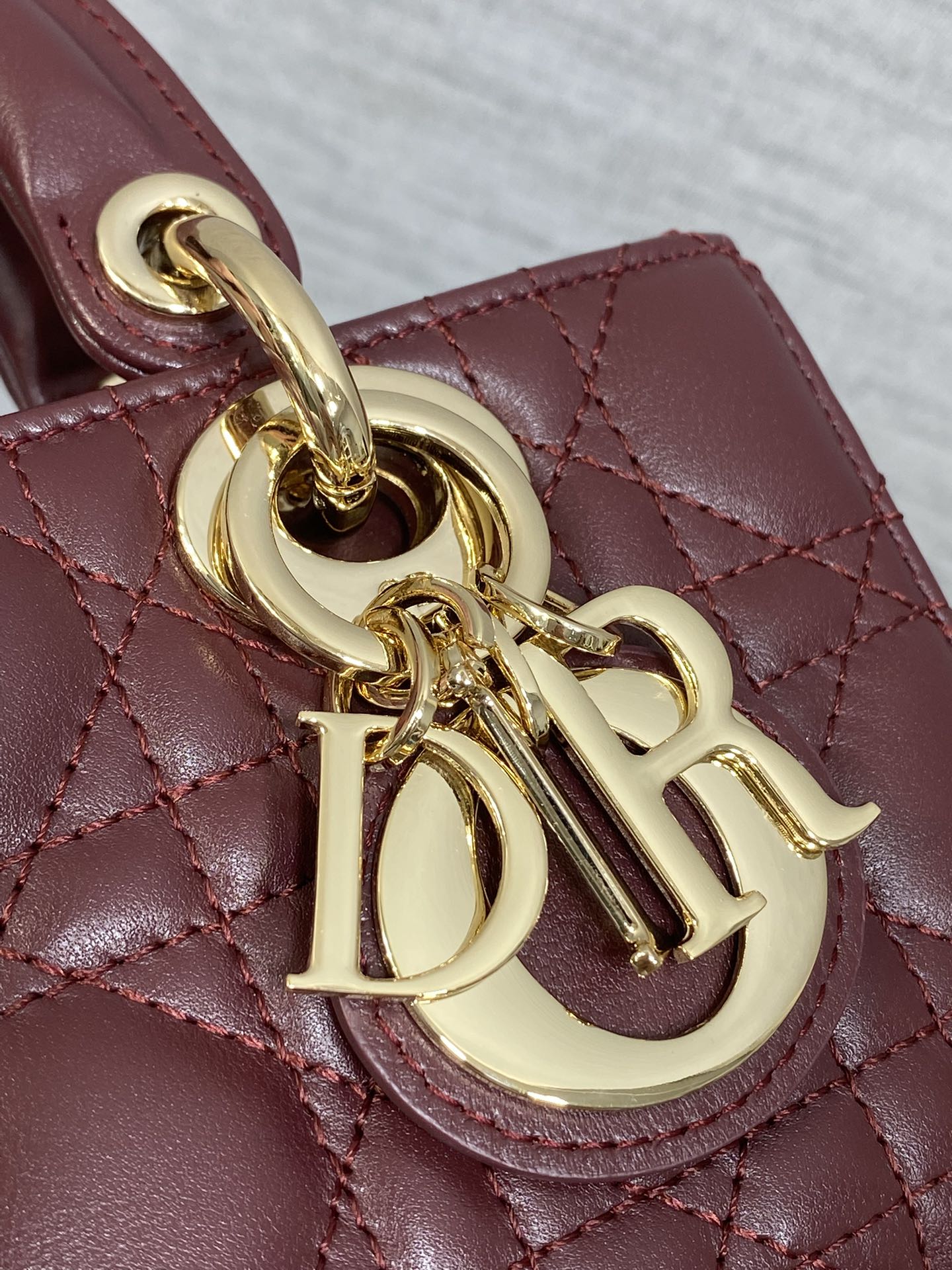 Dior logo charm close-up on burgundy quilted handbag with gold chain hardware