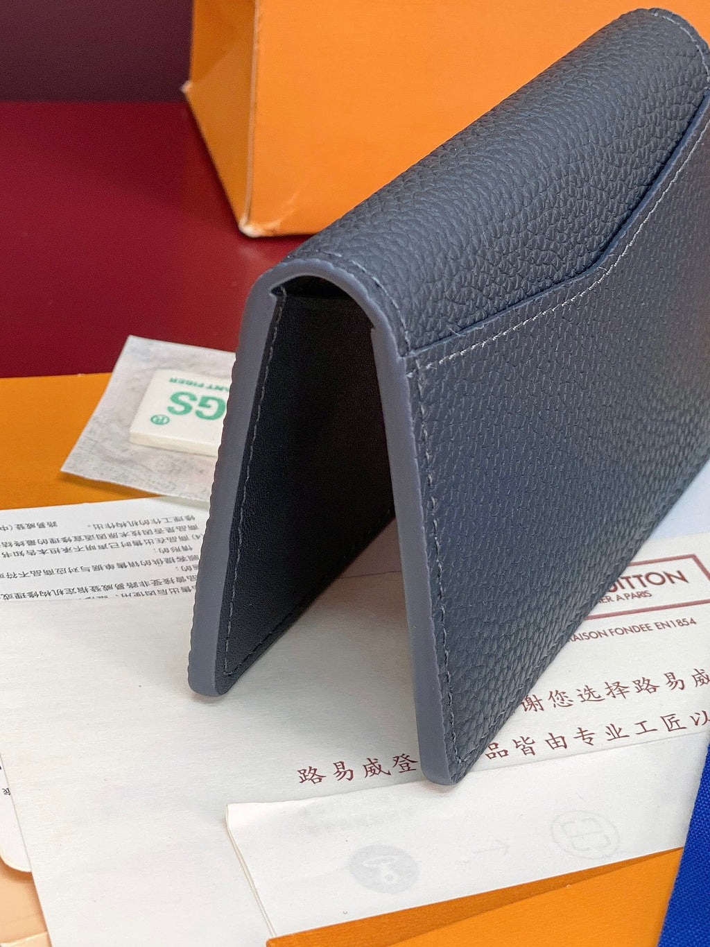 Small Louis Vuitton leather card holder, angled side view with fold and dark blue leather