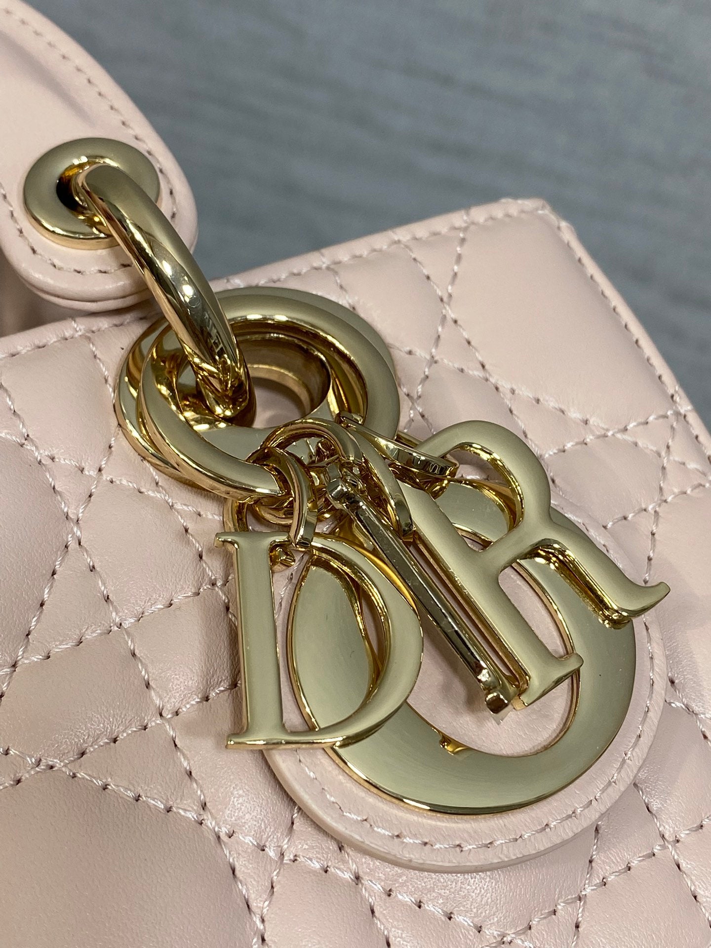 Close-up of pink Dior bag charm and gold chain hardware on quilted leather