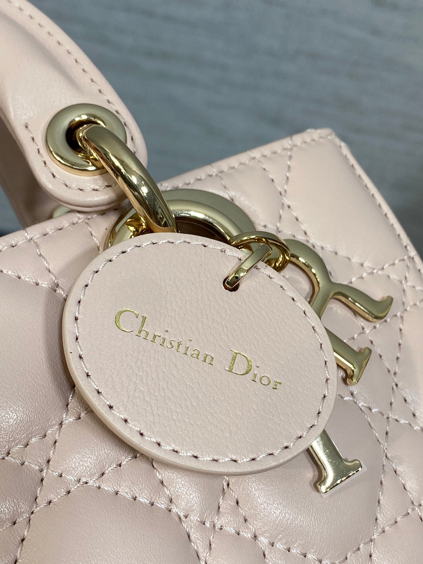 Close-up of Christian Dior oval charm tag on pink quilted bag with gold hardware