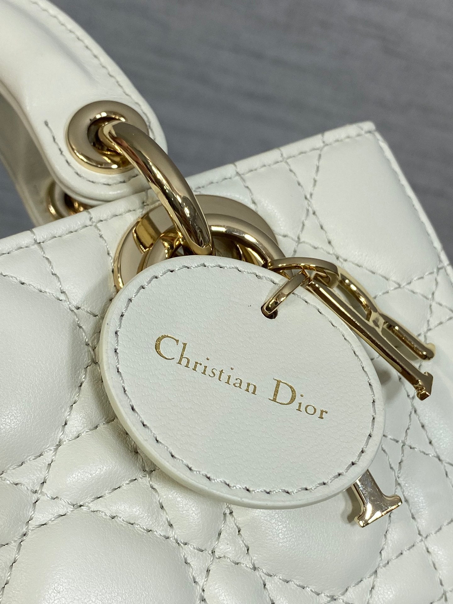 White quilted handbag charm with round Dior logo plaque and gold chain hardware
