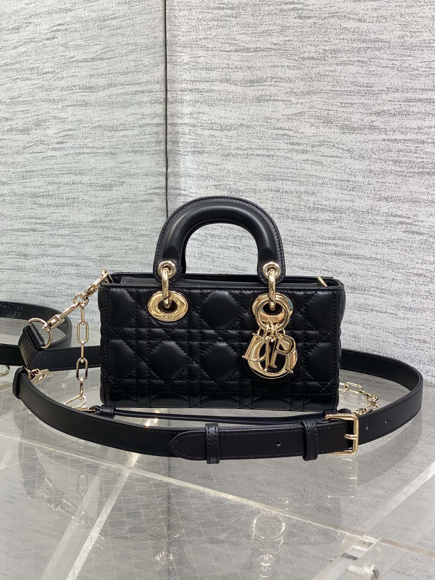 Dior quilted handbag in dark leather with top handles, gold logo charm, and crossbody strap