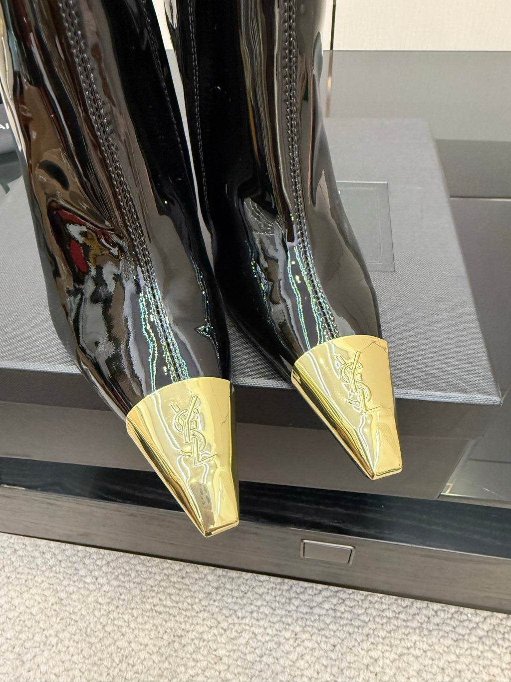 Close-up of black patent boots showing pointed gold heel tips