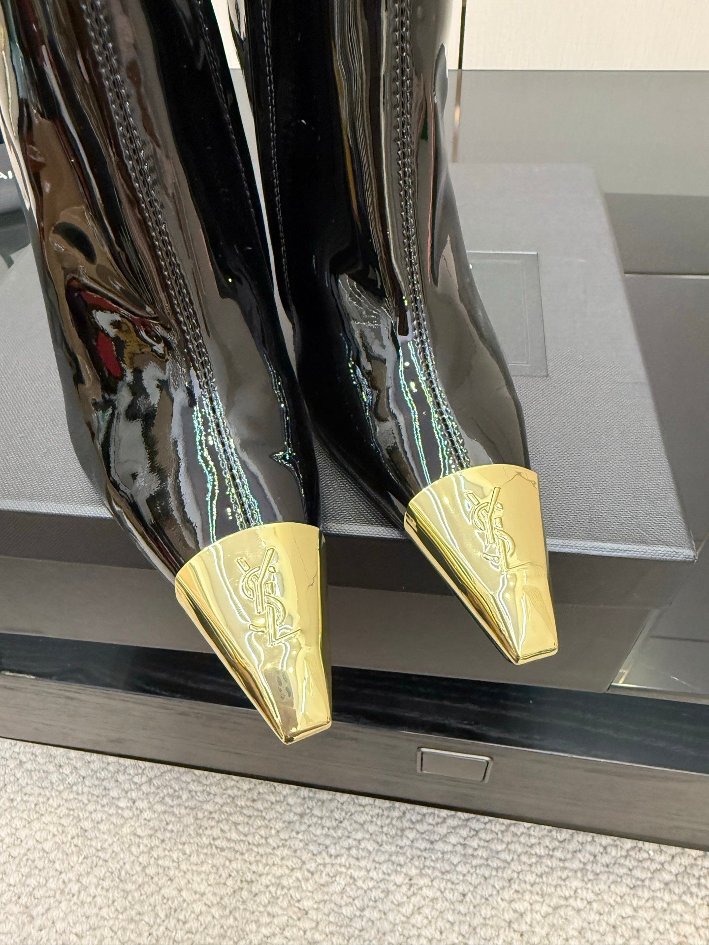 Close-up of black patent boots showing pointed gold heel tips