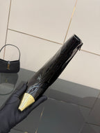 Black patent ankle boot held by gray-gloved hand, pointed gold toe