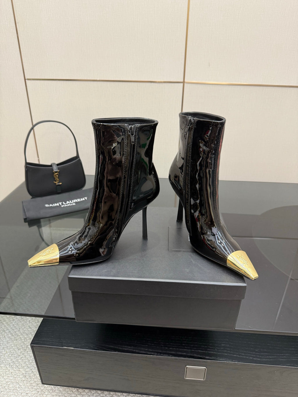 Black patent ankle boots with pointed gold heels, side-by-side on display stand