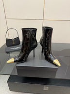 Black patent ankle boots with pointed gold heels, side-by-side on display stand