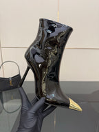 Black patent ankle boot with pointed gold heel tip held in gray glove