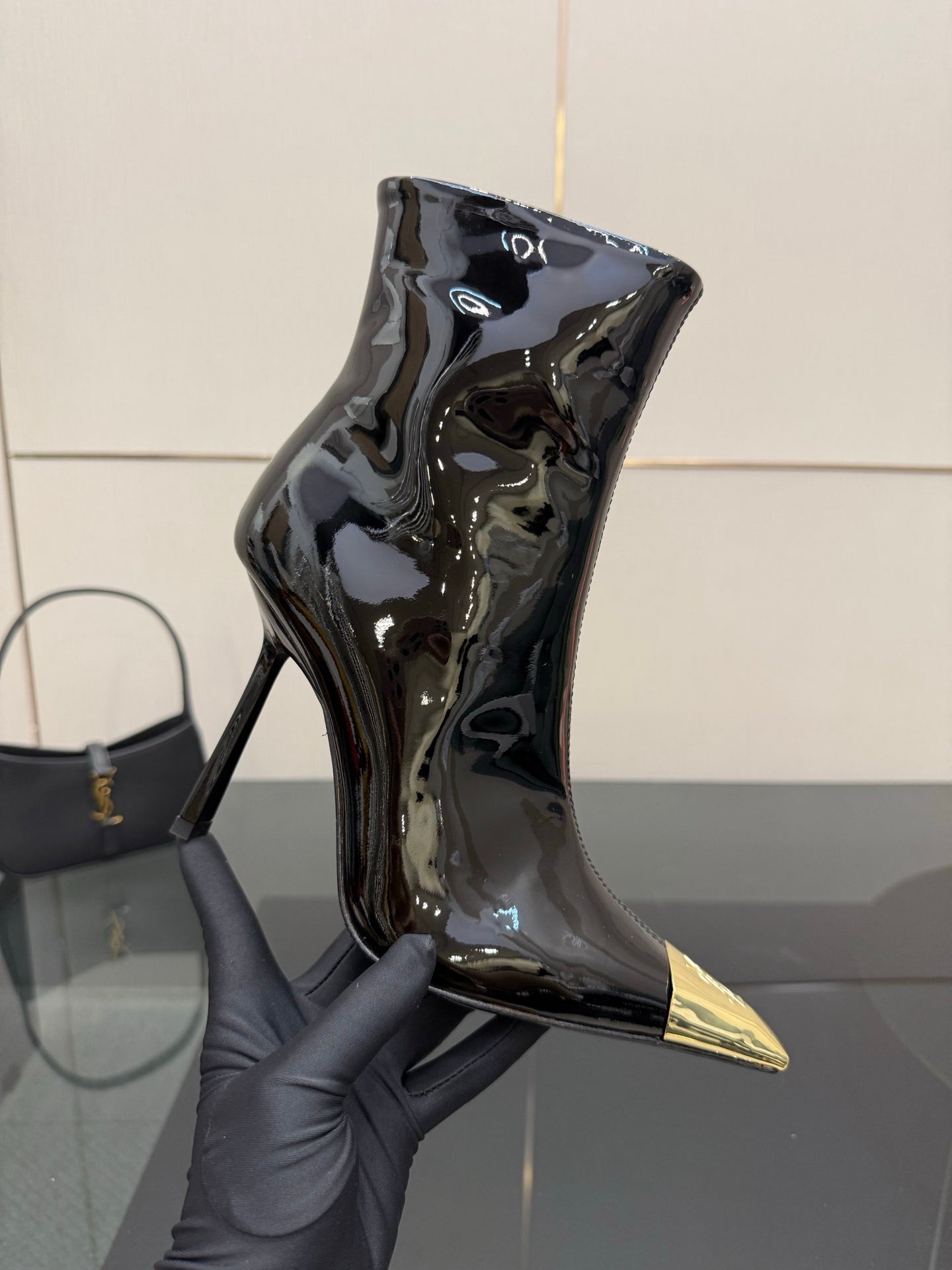 Black patent ankle boot with pointed gold heel tip held in gray glove