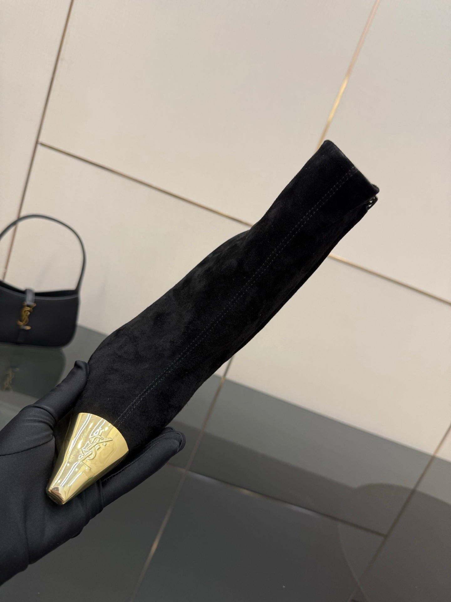 YSL women’s black suede boot held upright, pointed gold-tone toe cap visible