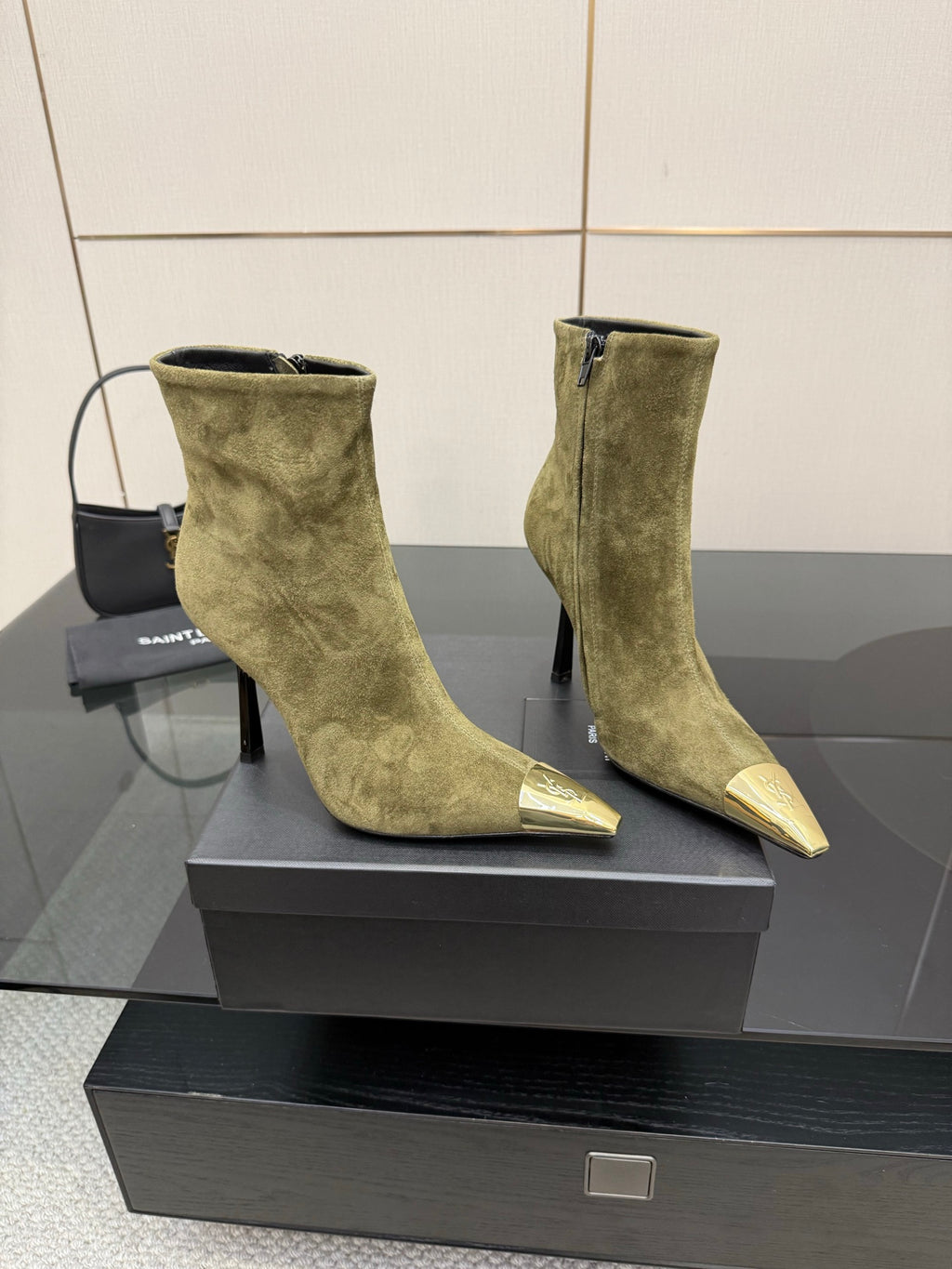 Two ladies’ olive suede ankle boots on a box, showing pointed gold-tone toe caps