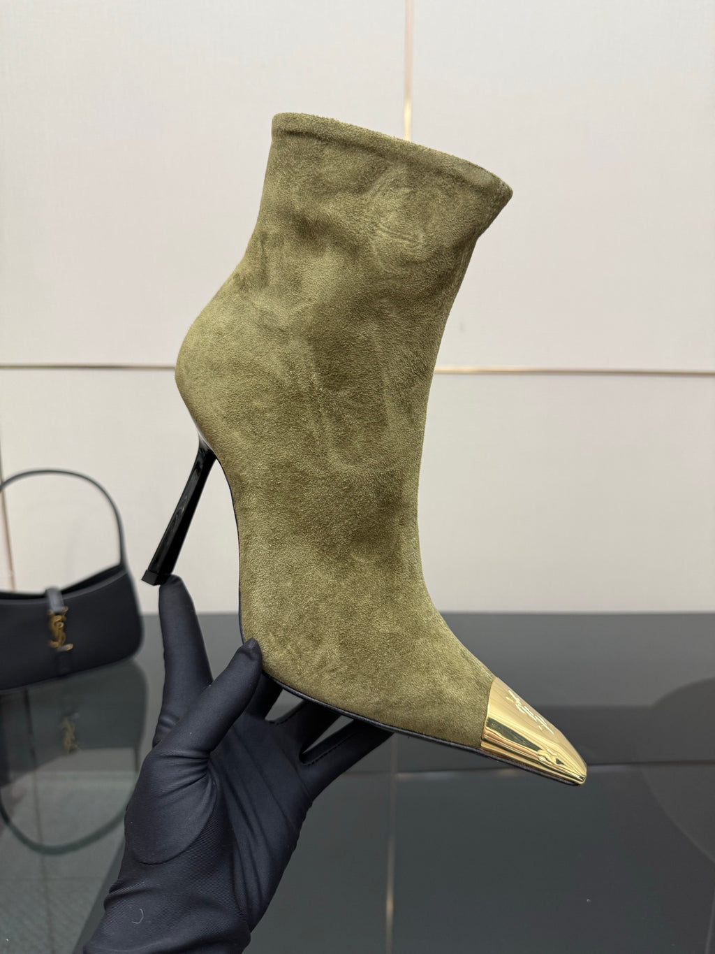 Ladies’ olive suede ankle boot on a hand, featuring pointed gold-tone toe and slim heel