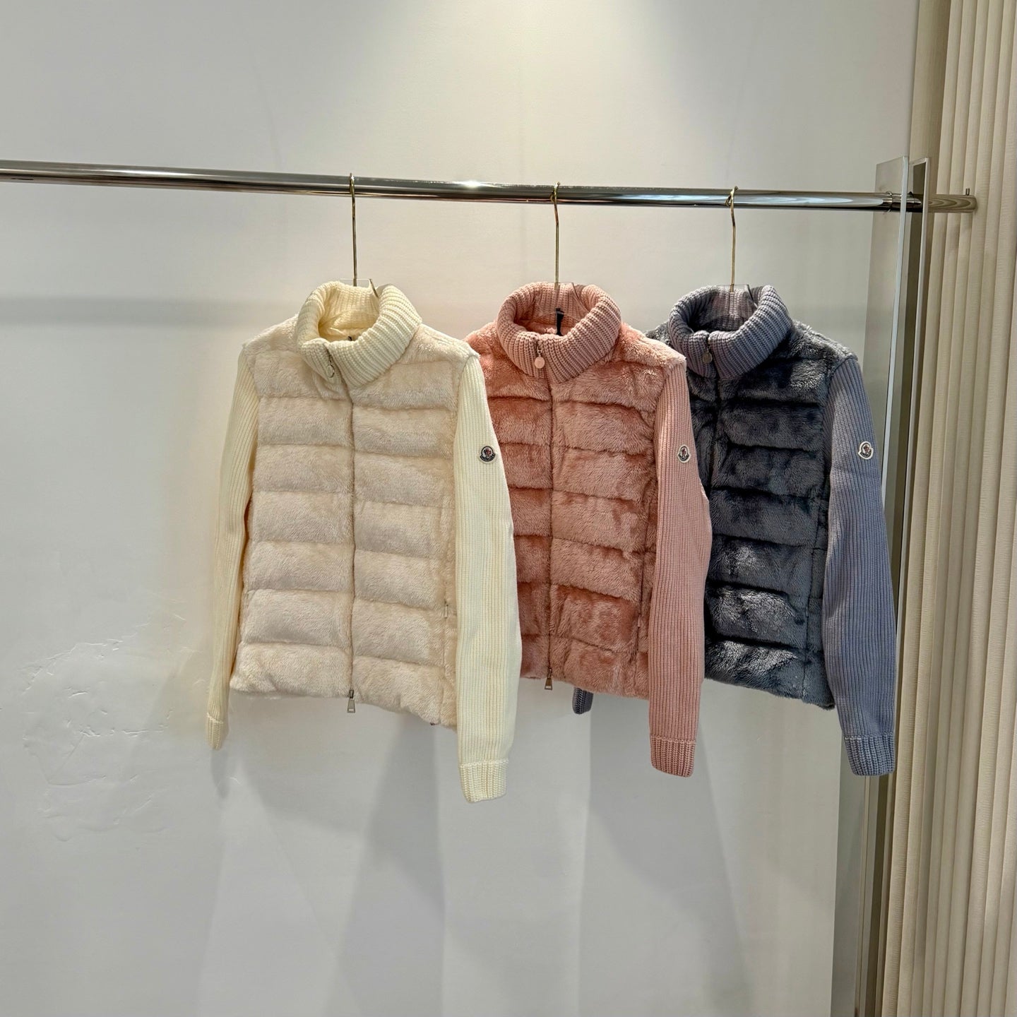 Long puffer jackets in cream, pink, and dark blue, knit collar visible.