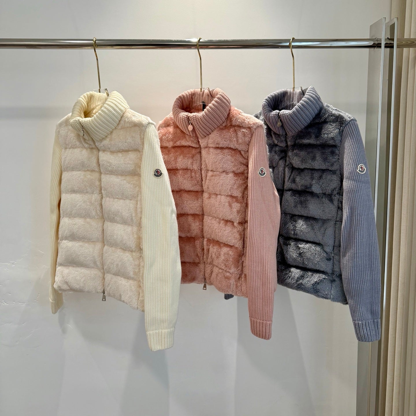 Long puffer jackets on rack: cream, pink, and dark blue with knit turtlenecks.