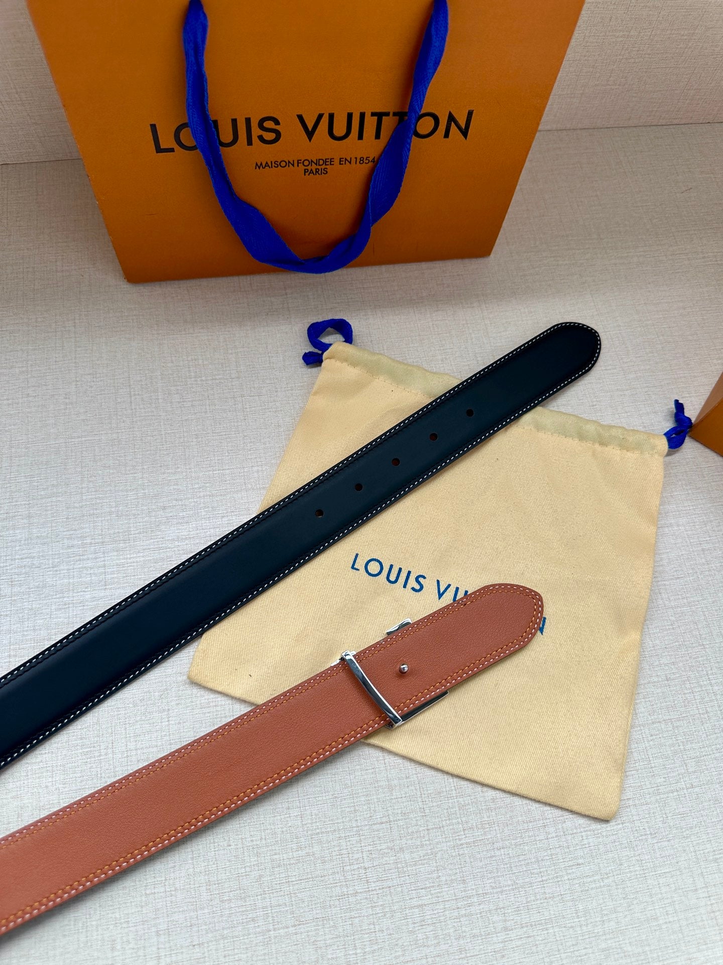 Navy and tan leather belts with metal buckles, laid flat