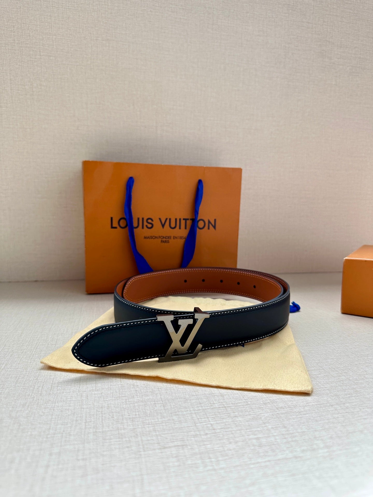 Navy leather belt with gold LV buckle, resting on a dust bag