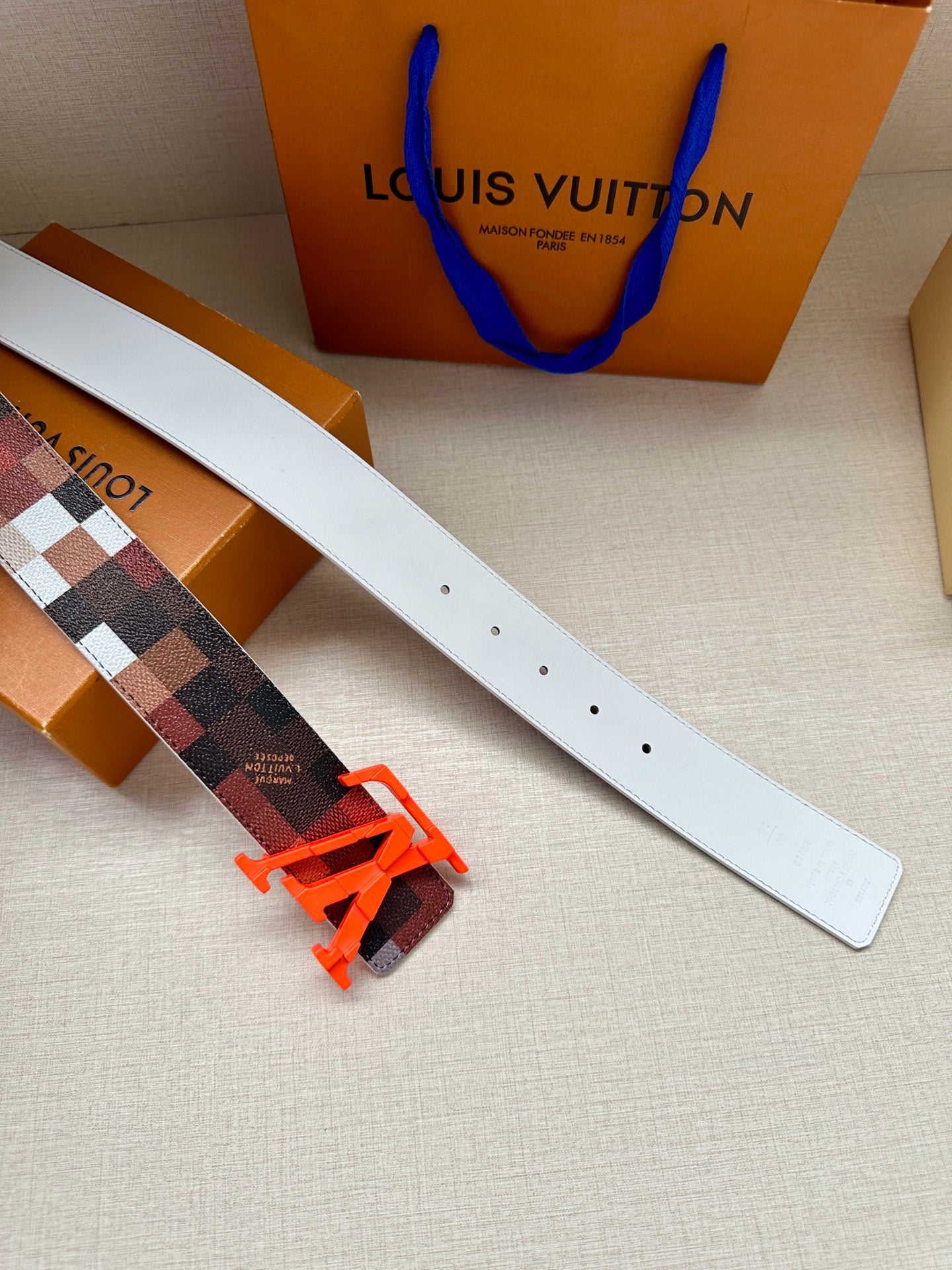 Louis Vuitton belt with white leather band, dark checkered strap, orange LV buckles